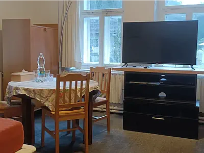 Kulatý stůl se židlemi a televize na černé skříňce u okna