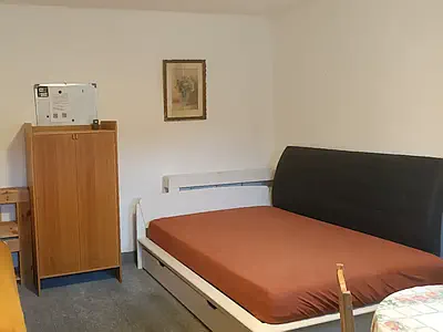 Zařízený pokoj s manželskou postelí, dřevěnou skříní a obrazem na stěně