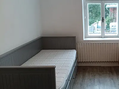 Šedá postel s matrací v rohu světlého pokoje